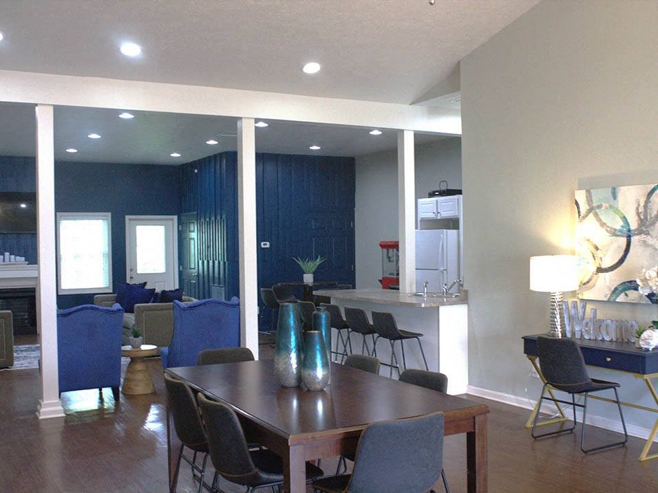 a room with a table and chairs and a kitchen in the background