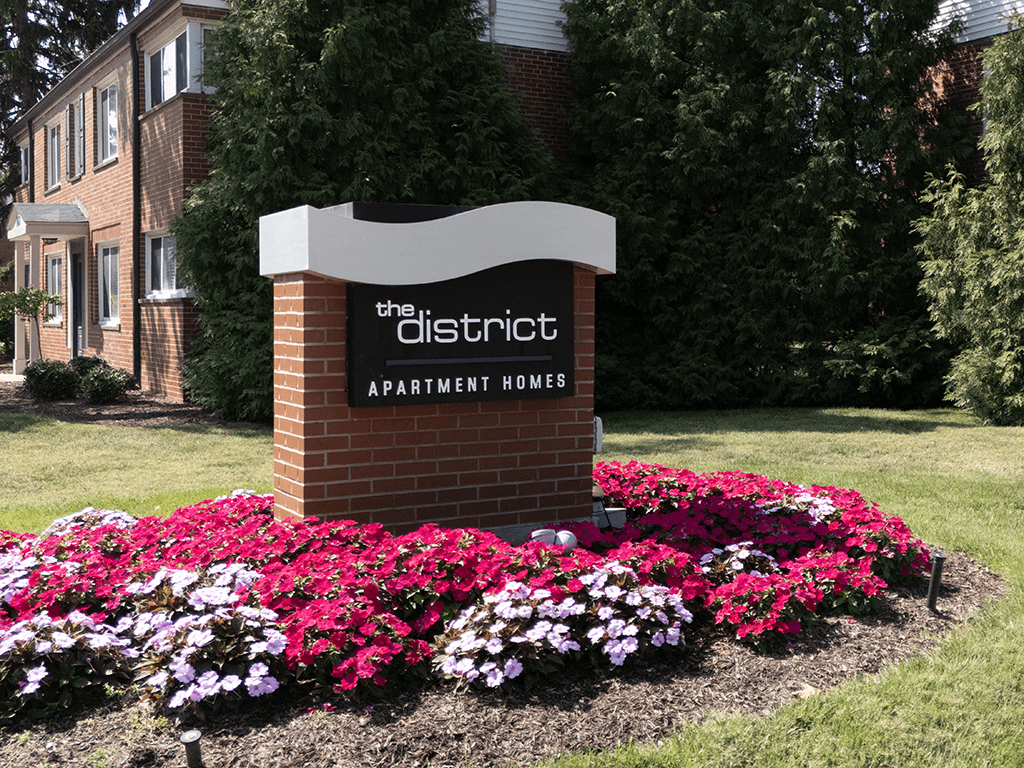 a sign for the district apartment homes in front of flowers