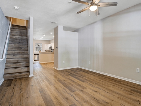 the living room and staircase of a new home with wood floors and a ceiling fan