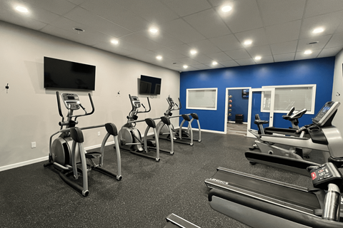 A gym with treadmills, exercise bikes, and a television.