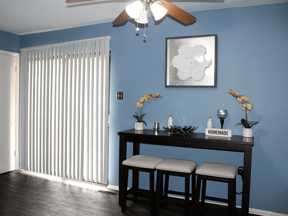 a dining room with a table and chairs in front of a blue wall with a ceiling fan