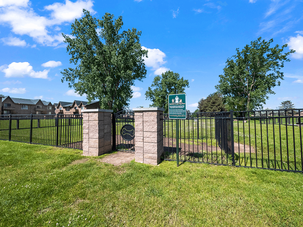 A green sign is on a gate in front of a grassy area.