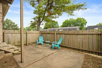 a patio with two chairs and a table in front of a fence