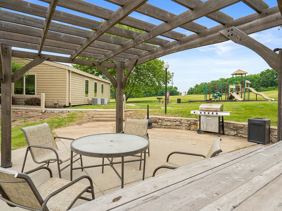 a patio with a table and chairs and a playground in the background