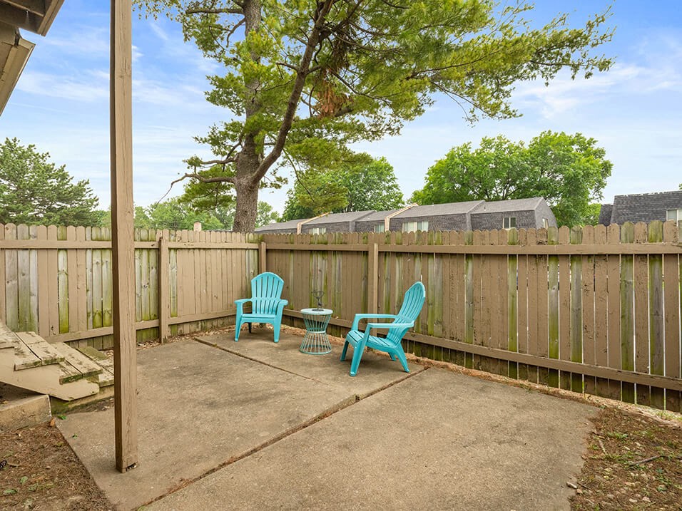 a patio with two blue chairs and a table in front of a fence