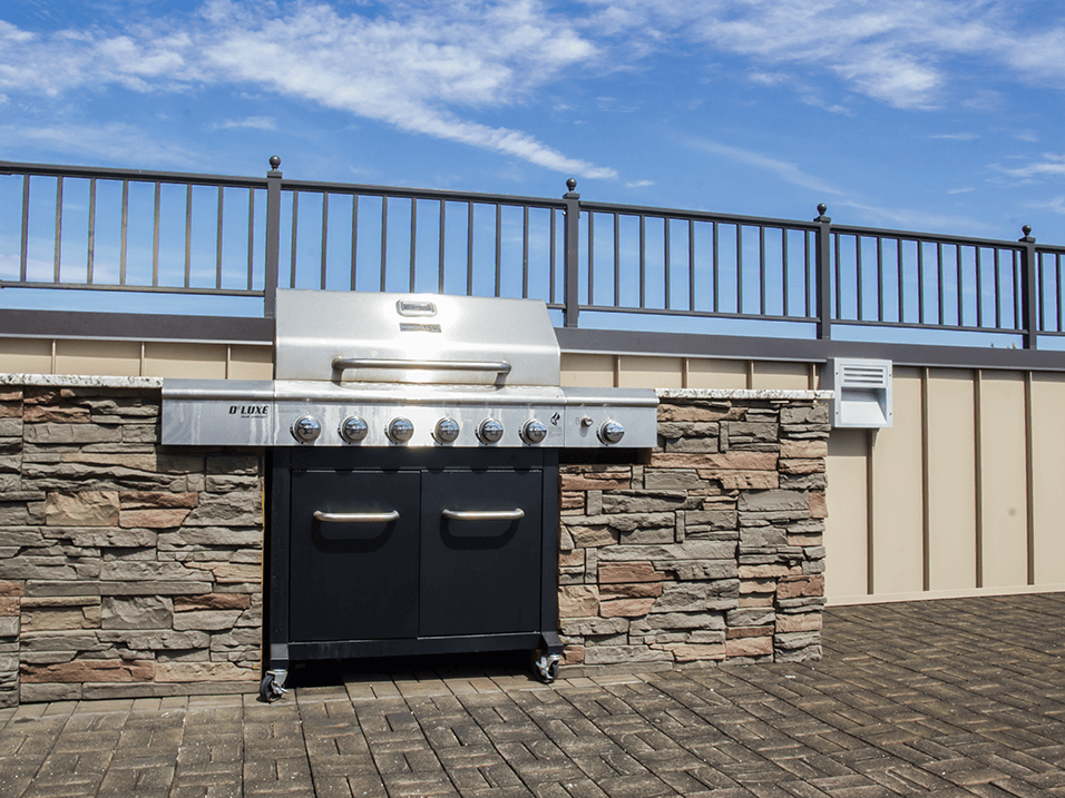 an outdoor barbecue grill with a stone wall and a metal railing