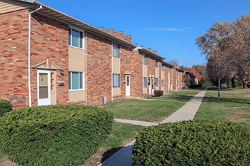 A row of red brick apartment buildings with green bushes in front.