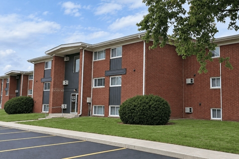 A red brick apartment building with a parking lot in front.