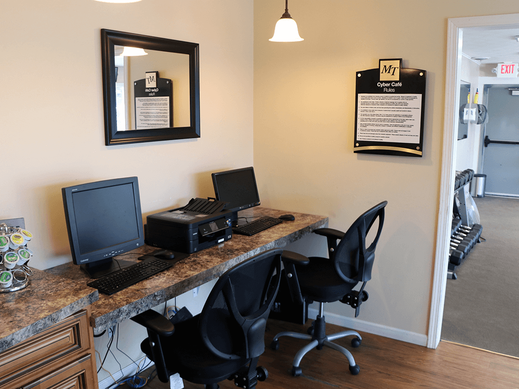 A black computer monitor and keyboard on a desk with a black chair.