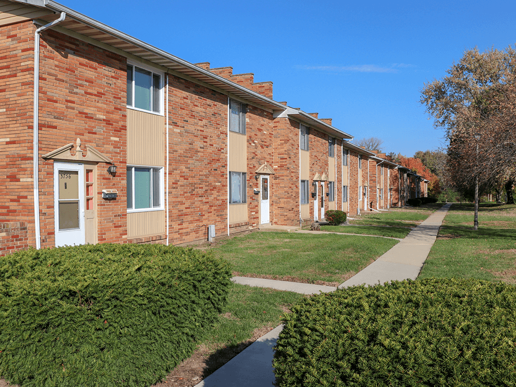 A row of red brick apartment buildings with green bushes in front.