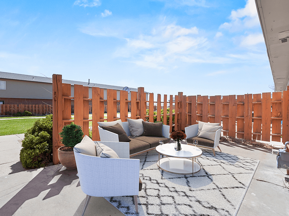 a patio with two couches and a coffee table in front of a wooden fence