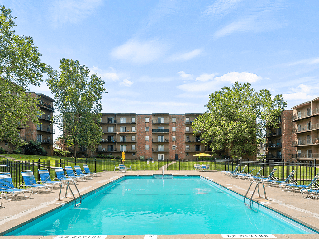 a swimming pool with blue chairs and a building in the background