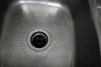 A close up of a sink drain with water droplets on it.