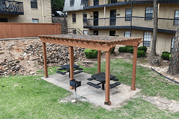 A wooden pergola with a bench is in the middle of a grassy area.