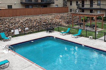 A small pool surrounded by a black fence with two chairs and a table.