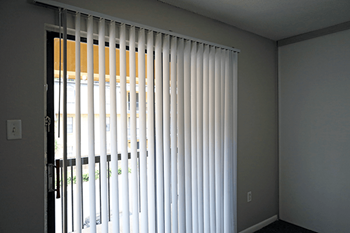 A room with a window covered by white vertical blinds.