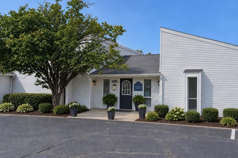 A white building with a black door and a tree in front.