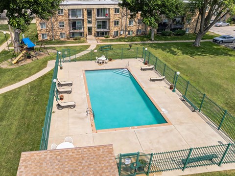 A green fenced in pool with a building in the background.