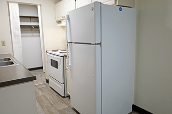 A white refrigerator stands in a kitchen with a sink and stove.