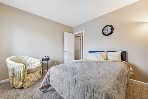 A bedroom with a bed, a chair, and a clock on the wall.