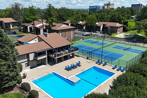 A tennis court surrounded by a pool and apartment buildings.