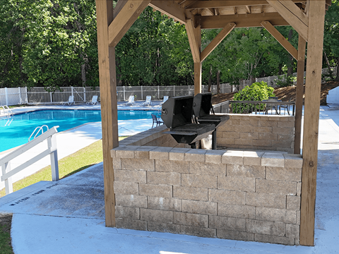 A wooden pergola with a grill is situated next to a pool.