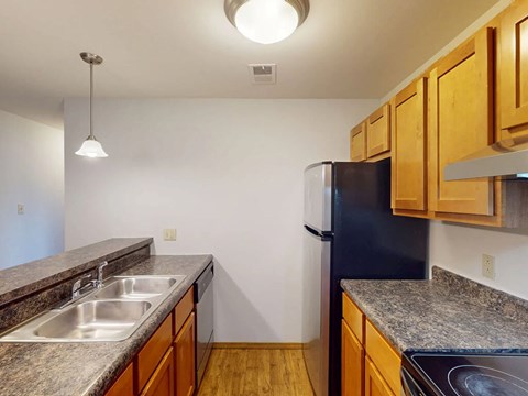 A kitchen with a black refrigerator and wooden cabinets.