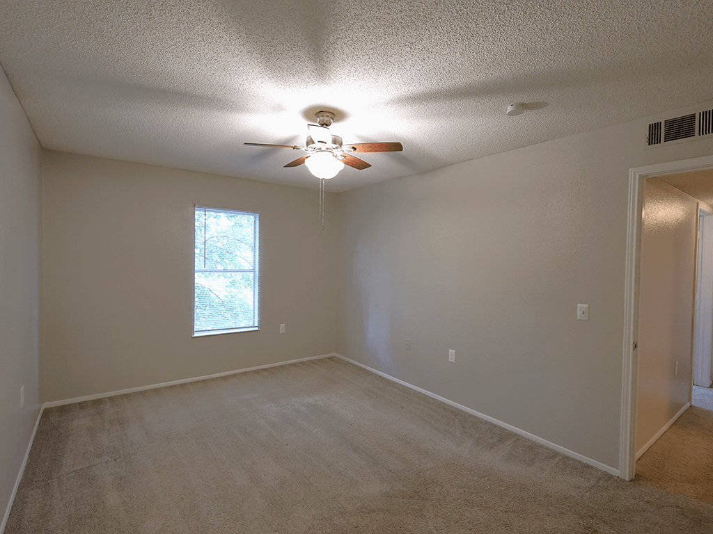 an empty living room with a ceiling fan and a window