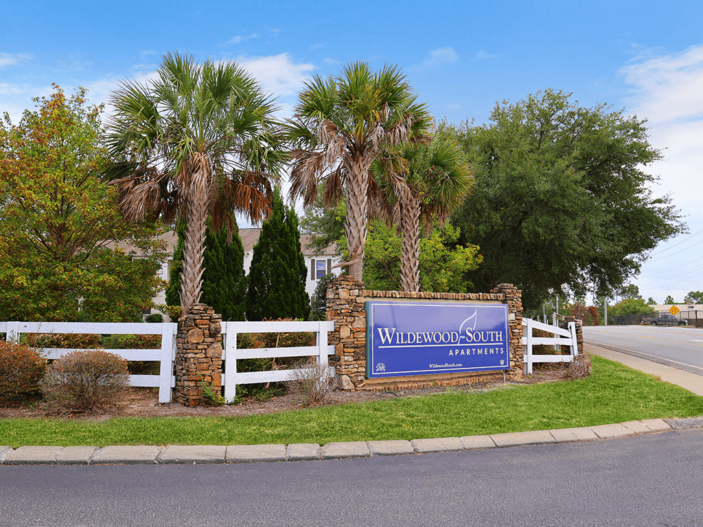 a sign in front of palm trees and a white fence