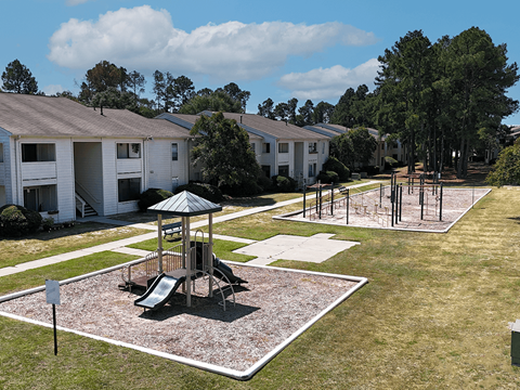 A playground area with a slide and a swing set in the middle of a grassy area.