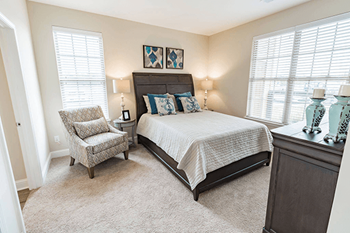 A bedroom with a bed, chair, and two lamps.