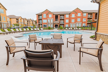 A pool surrounded by chairs and tables in front of apartment buildings.
