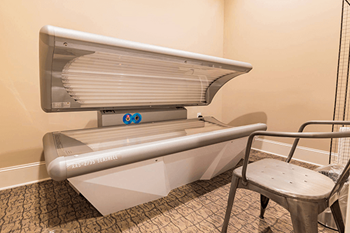 A tanning bed with a metal frame and a white cover is in a room with patterned carpeting.