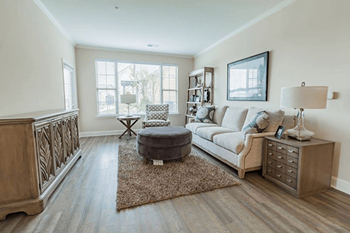 A living room with a grey ottoman, a white sofa, and a wooden sideboard.