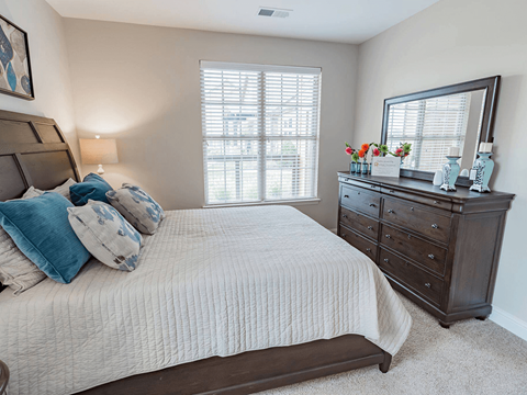 A bedroom with a large bed, a dresser, and a window with blinds.