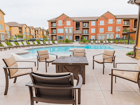 A pool surrounded by chairs and tables in front of apartment buildings.