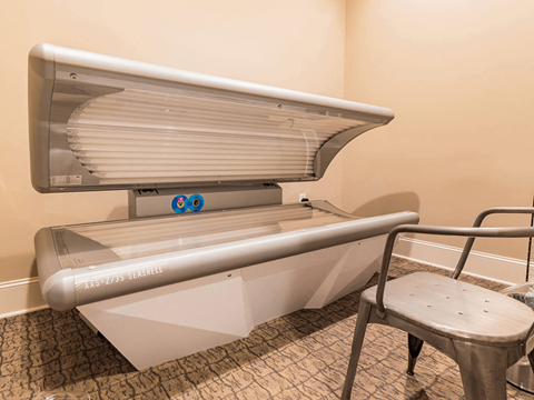 A tanning bed with a metal frame and a glass enclosure is in a room with a patterned carpet.