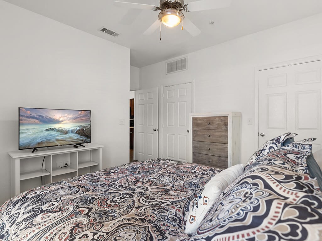 A bedroom with a bed, a television, and a ceiling fan.