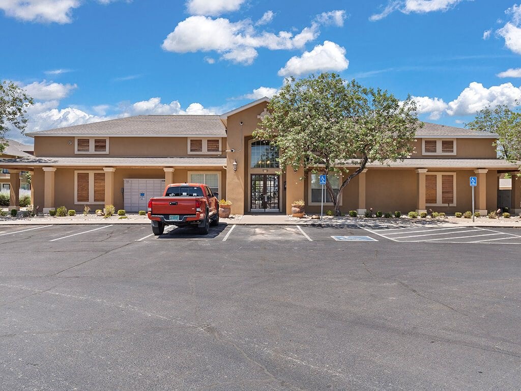 A red truck is parked in front of a building with a tree in front of it.