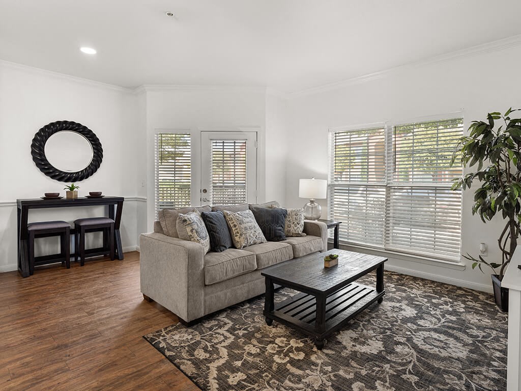 A living room with a grey couch, a coffee table, and a mirror on the wall.