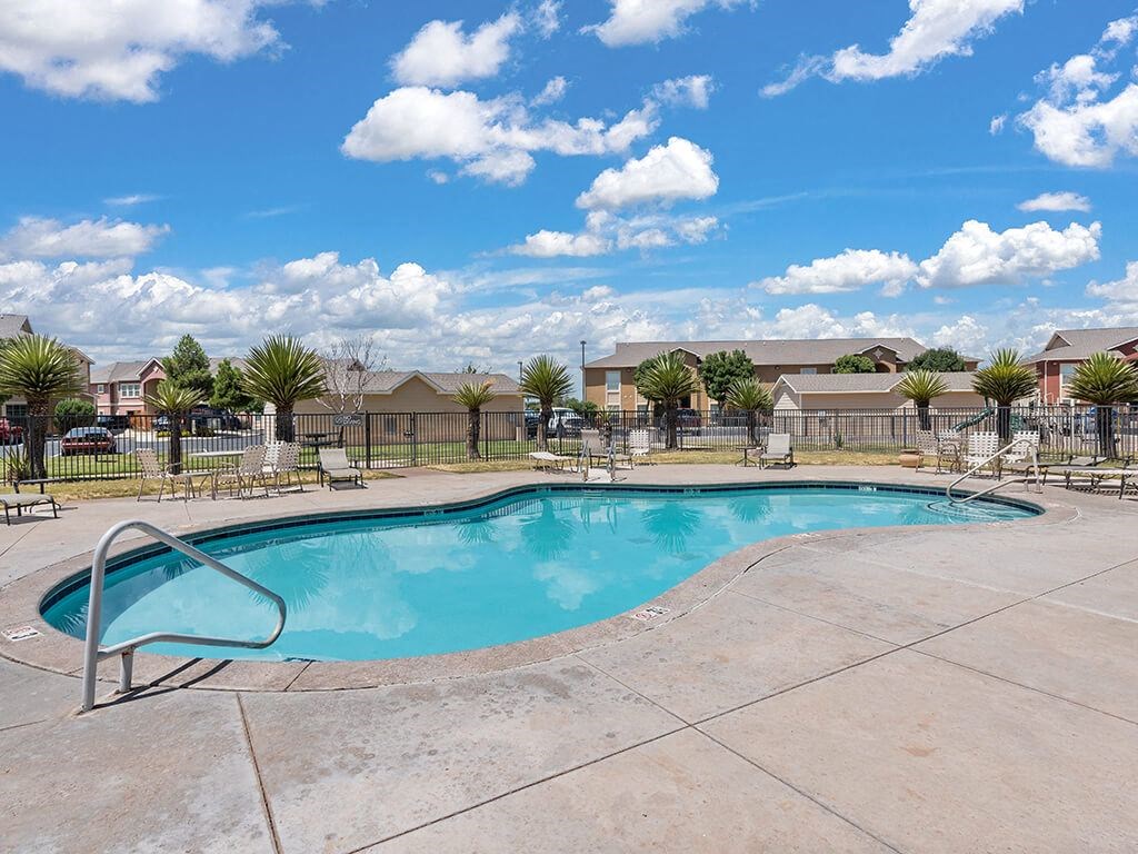 A swimming pool surrounded by a concrete patio and a metal fence.