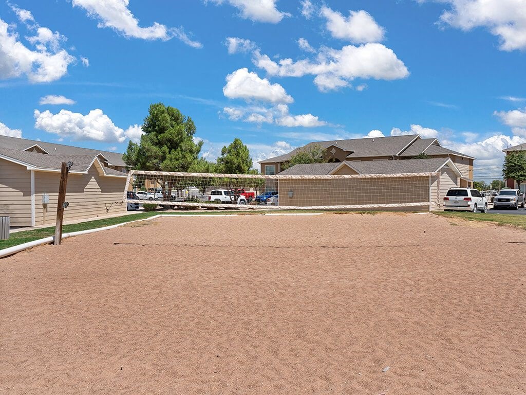 A sandy area with a few buildings and cars in the background.