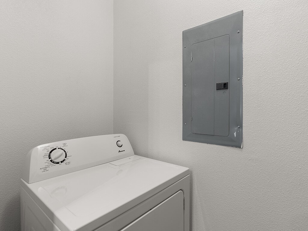 A white washing machine sits next to a wall-mounted electrical panel.