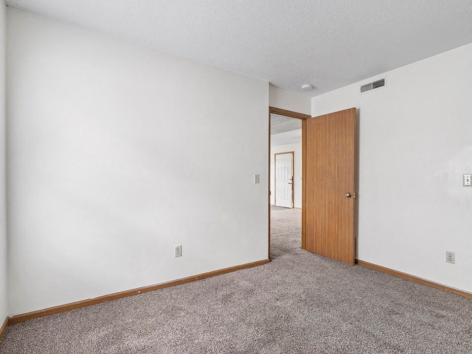 a carpeted bedroom with white walls and a wooden door