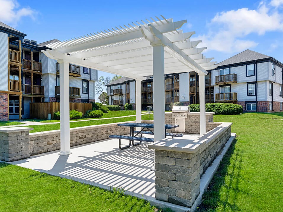 a pergola with a picnic table in front of an apartment complex