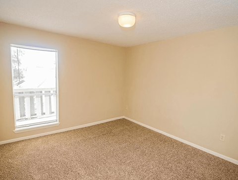 an empty bedroom with a window and carpet
