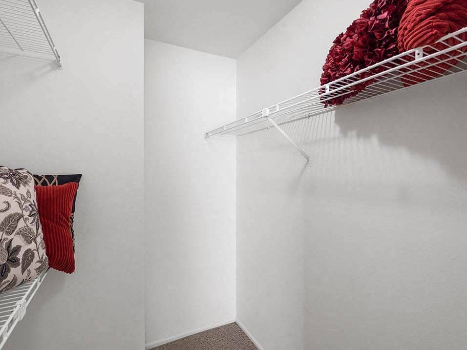 a walk in closet with a white wall and a wire rack on the wall