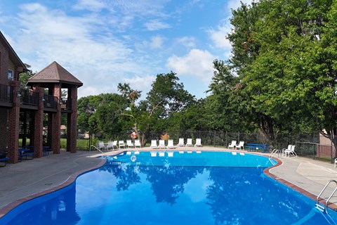 A large blue swimming pool with white lounge chairs and a gazebo in the background.