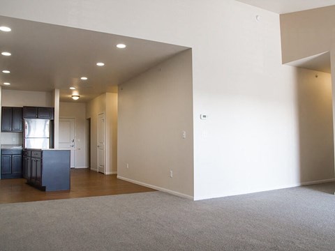 an empty living room with a kitchen in the background