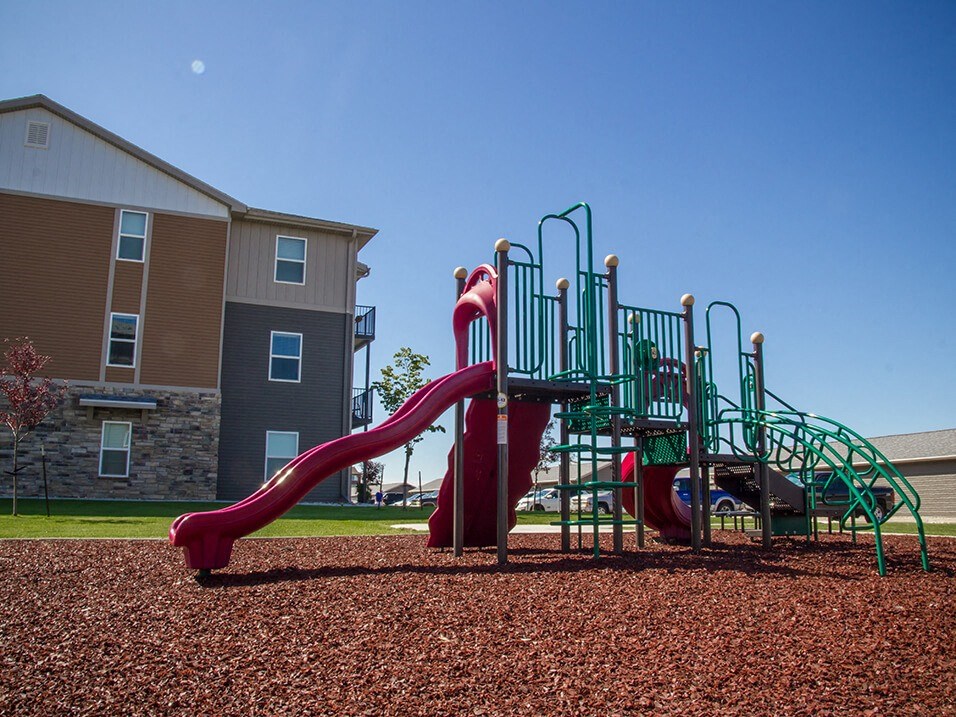 a playground with a slide and climbing equipment in front of an apartment building
